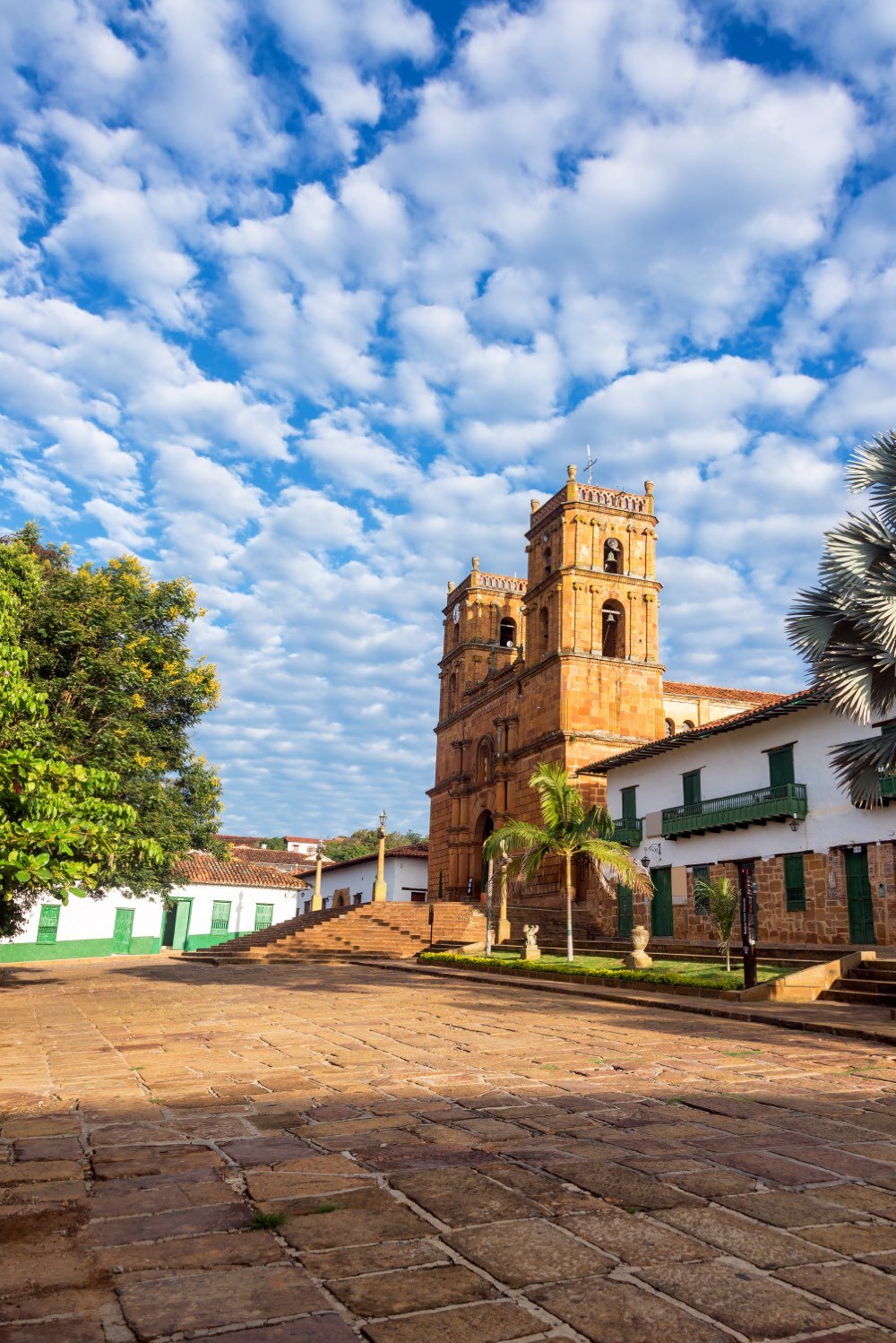 Fachada de piedra de la catedral de la Inmaculada Concepción de Barichara con sus dos torres, bajo un cielo azul con nubes