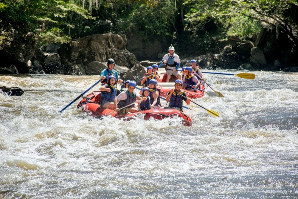Balsa de rafting con varios pasajeros atravesando un rápido embravecido del río Fonce, entre paredes de roca y vegetación densa