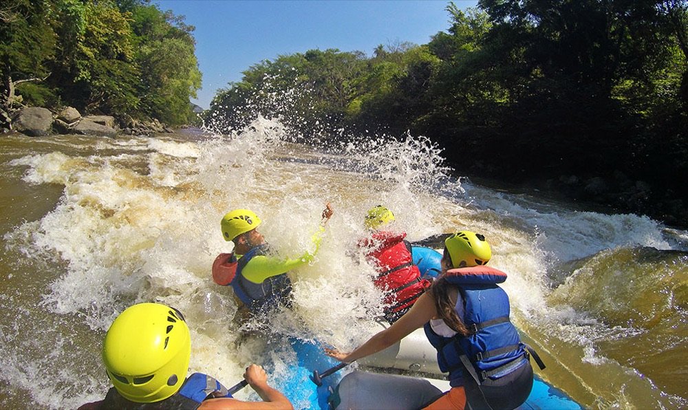 Grupo de rafting con cascos amarillos atravesando una ola grande en un rápido del río Fonce