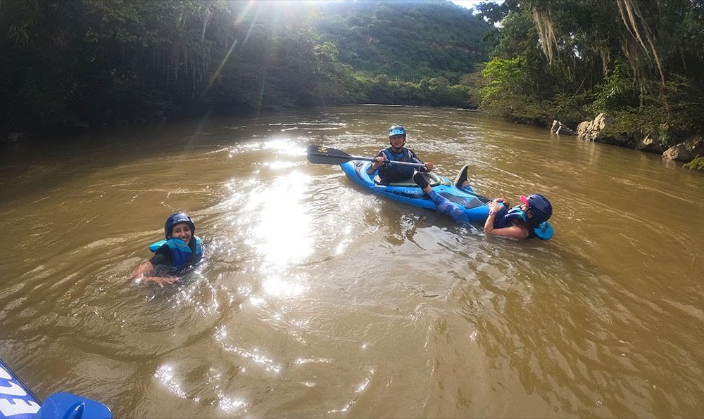 Turistas flotando en aguas tranquilas del río Fonce junto a un kayak, con la selva de galería en la ribera