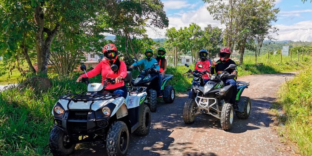 Grupo de cinco personas en tres cuatrimotos posando en un camino rural rodeado de árboles, con las montañas de Santander al fondo