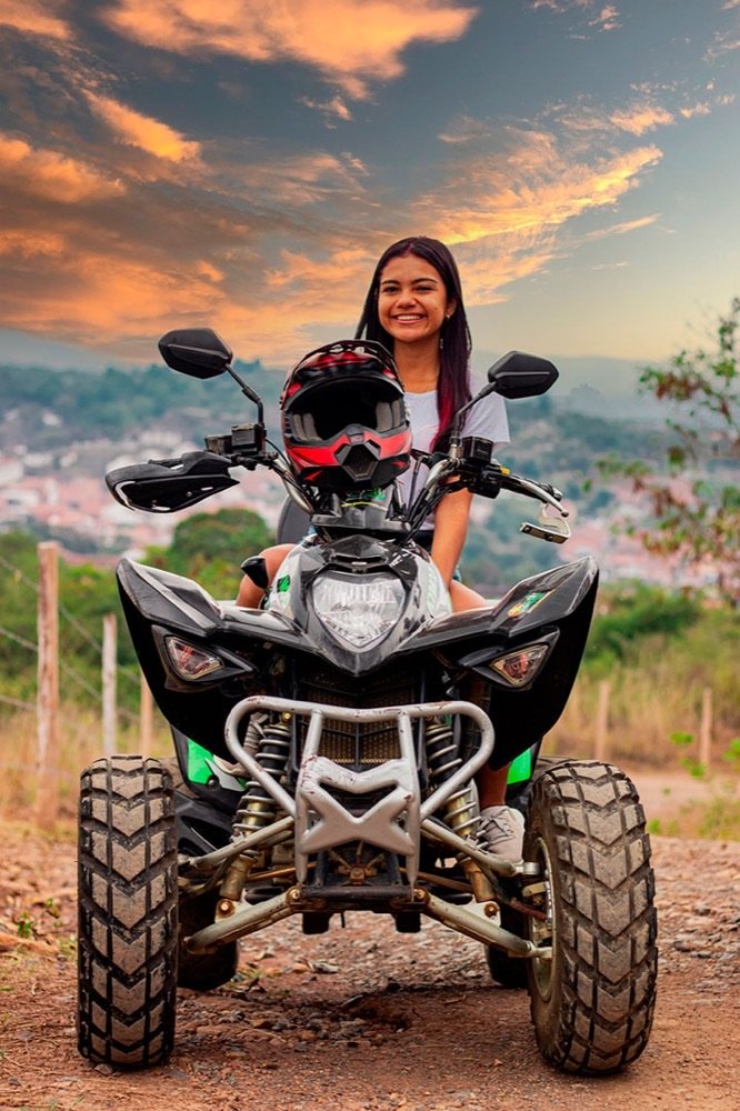 Mujer sonriente montada en un cuatrimoto con el pueblo de San Gil y un cielo de atardecer anaranjado de fondo