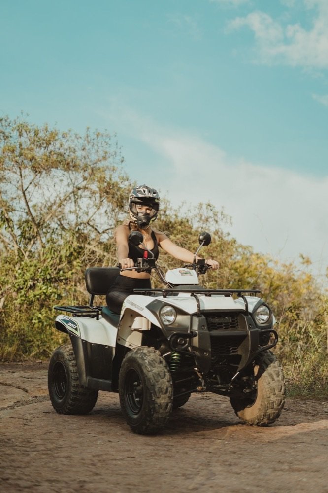 Mujer con casco integral conduciendo un cuatrimoto blanco por un camino de tierra rodeado de vegetación