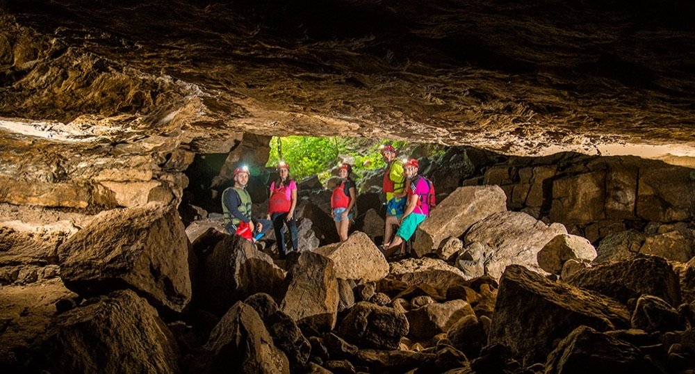 Grupo de espeleólogos de pie sobre rocas a contraluz en la entrada de la Cueva del Indio, con la selva verde visible afuera
