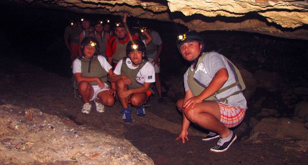 Grupo de espeleología con cascos y linternas frontales agachados dentro de una cueva de San Gil