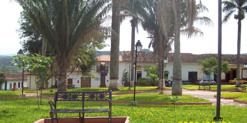 Parque principal de Curití con altas palmeras, una banca de hierro y casas coloniales blancas de tejado rojo al fondo