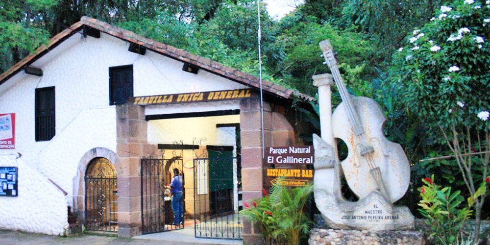 Entrada del Parque Natural El Gallineral con la taquilla, el letrero del restaurante-bar y una escultura de tiple en piedra