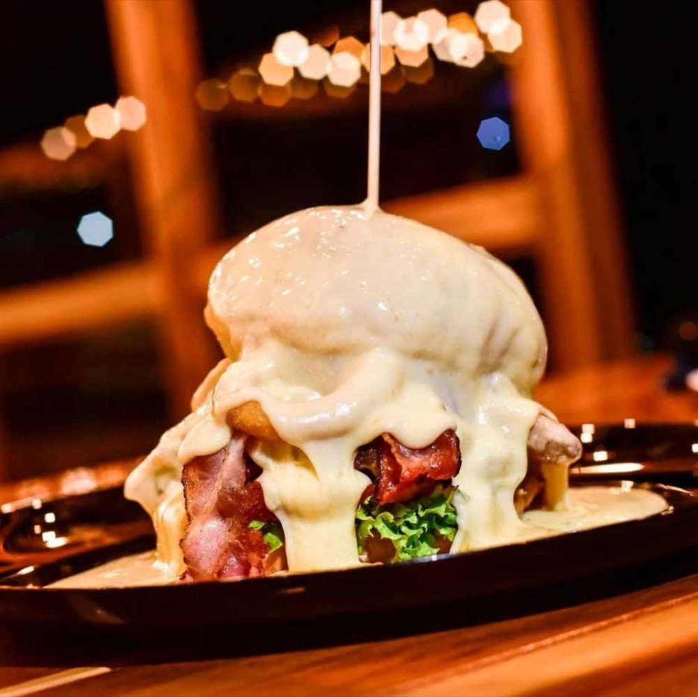 Hamburguesa gourmet cubierta con queso fundido derramándose sobre tocineta y lechuga, servida en un plato oscuro