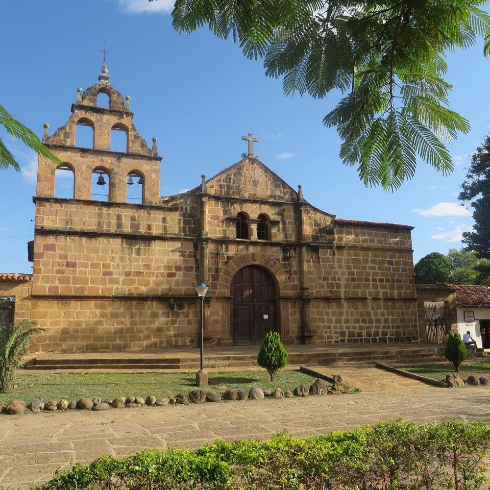 Fachada colonial de piedra de la iglesia de Guane con su campanario de tres campanas, vista desde la plaza principal en un día despejado
