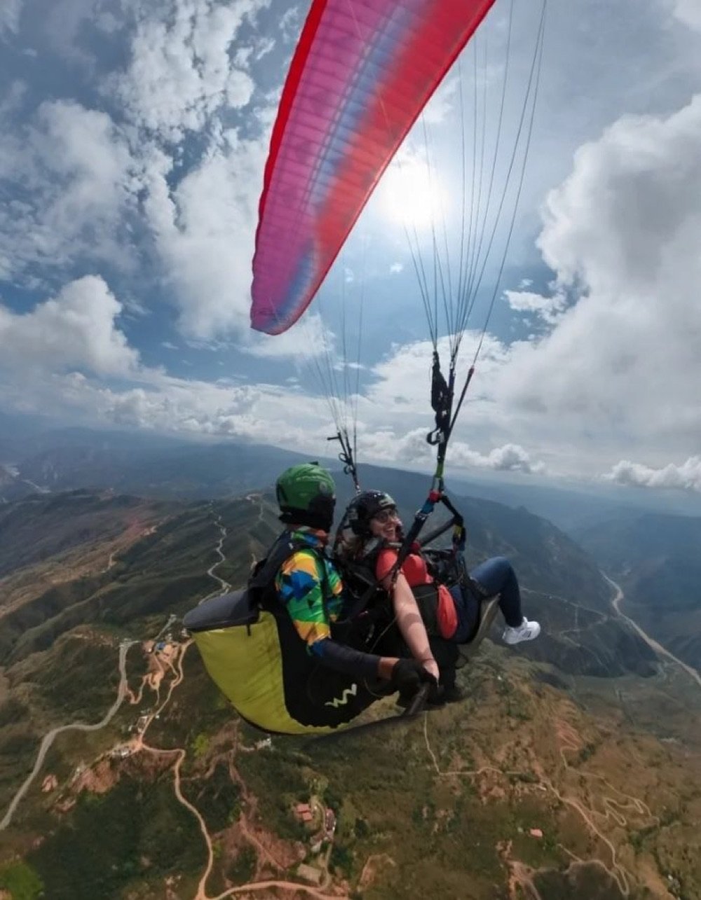 Parapente con vela roja y morada volando muy alto sobre el cañón del Chicamocha, con las paredes rocosas del cañón muy por debajo