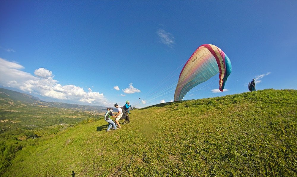 Equipo de vuelo preparando el despegue de un parapente en la cima de una colina en Curití, con el valle al fondo