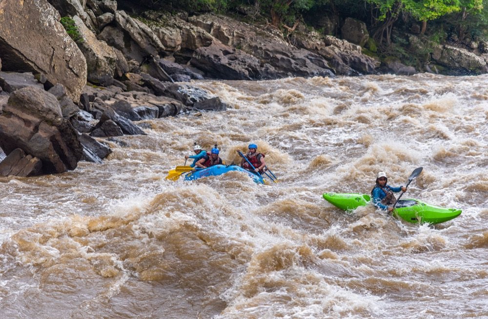 Balsa de rafting y un kayak de seguridad cruzando juntos un rápido caudaloso del río Suárez junto a una pared de roca