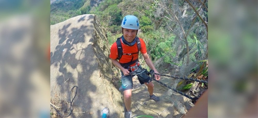 Hombre con casco y arnés descendiendo en rappel una pared de roca seca, con las cuerdas de seguridad tendidas sobre la ladera