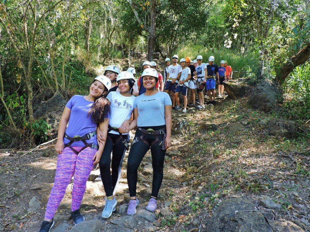 Grupo grande de excursionistas con casco caminando en fila por un sendero boscoso durante una caminata ecológica